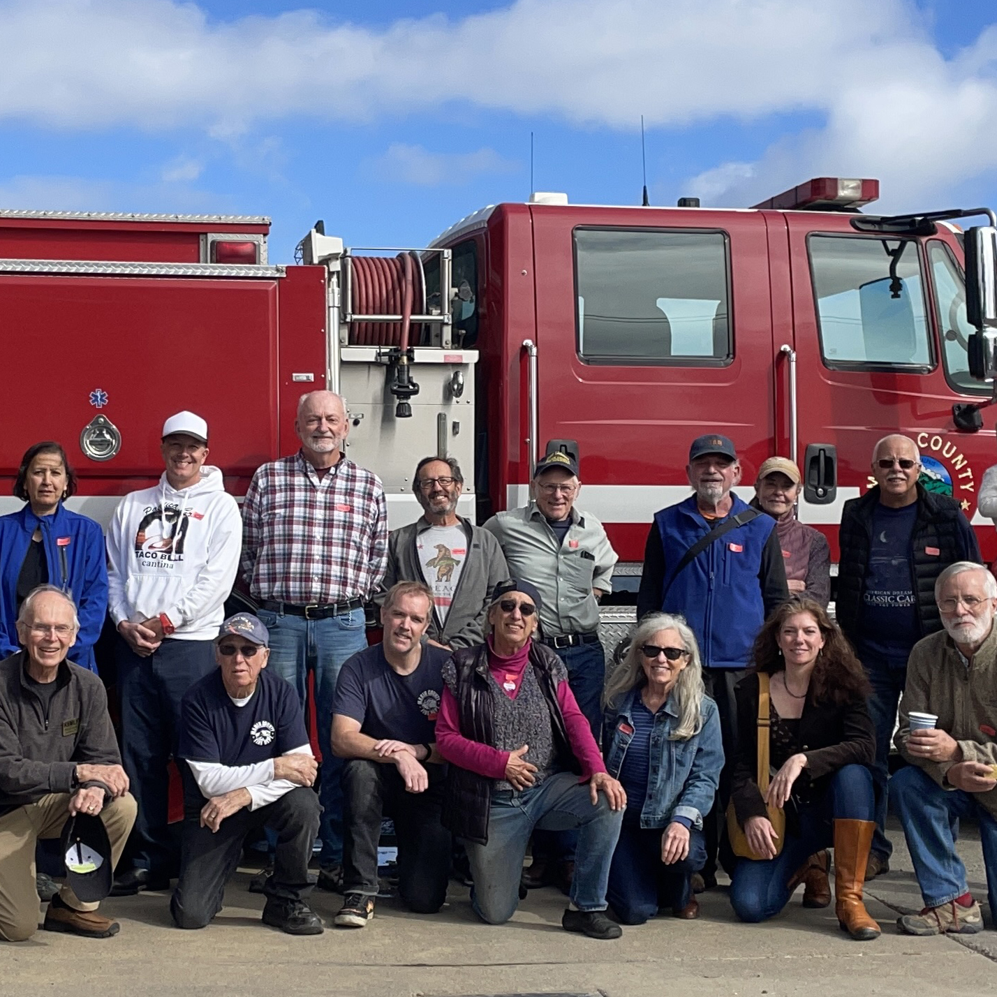A group of 4 volunteers wearing orange safety vests and holding a sign that says 'Lend a Hand'